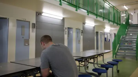 Getty Images Prisoner sitting at a table in the middle of a prison block on his own