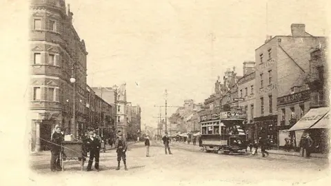 Courtesy of Peterborough Civic Society An old black and white picture of a street with a tram in the foreground and people standing at the corner of the street with carts.