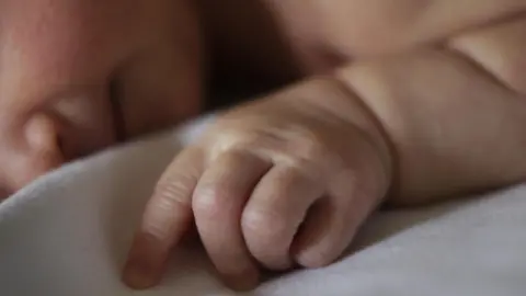 Danny Lawson/PA Wire A baby is lying sleeping on a blanket. 