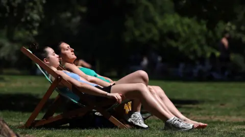 ANDY RAIN/EPA/Shutterstock Two people relax on lounge chairs in the sun outdoors.
