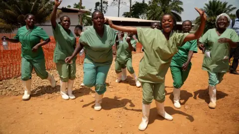 Health workers in green scrubs and white boots dancing in DR Congo
