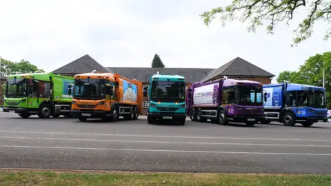 Five of the council's bin lorries parked side by side painted in bright green, orange, turquoise, purple and blue colours
