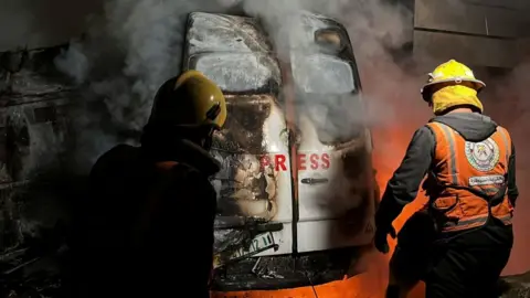 Gaza's civil defence members tackle a fire in a van with "Press" written on the back door following an Israeli strike in the Nuseirat refugee camp (26/12/24)