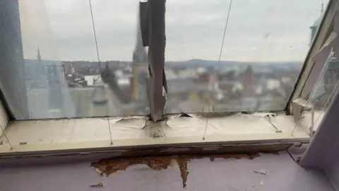 Simon Thake/BBC An old crumbling window frame looking out high above buildings in Sheffield