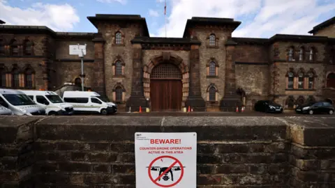 EPA The entrance to HMP Wandsworth, a stone building resembling a castle, with a low wall in front of it bearing a sign saying "Beware counter-drone operations active in this area" with a drawing of a drone with a red circle around it and a diagonal red line through it