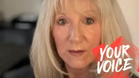 Tracy McGuire-Brown looks at the camera. She has cropped blonde hair, a pearl necklace and a black jumper.