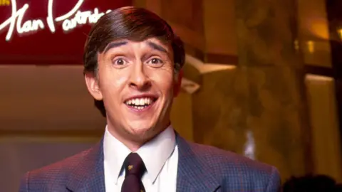 Steve Coogan as Alan Partridge looks animatedly at the camera with a sign behind him that reads "Knowing Me, Knowing You with Alan Partridge".