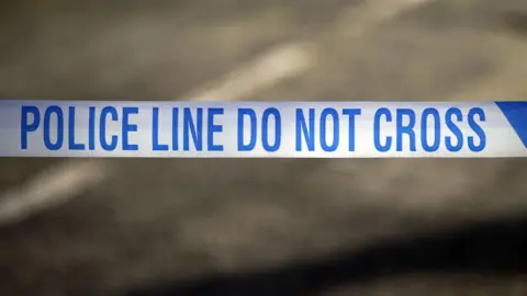 White police tape with blue writing saying Police Line Do Not Cross