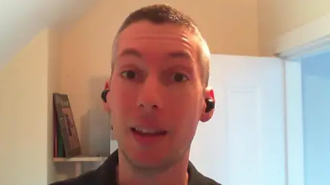 BBC News Sam Turner, a young man with cropped hair, sits speaking on Zoom. He has black earbuds in his ears. 