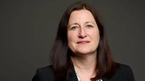 UK Parliament A woman with dark hair and a dark top in front of a dark grey background