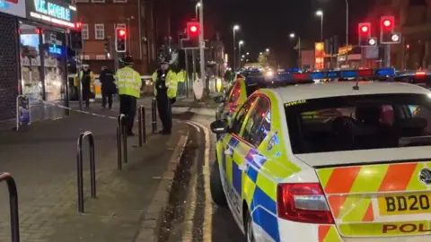 Leicester Media Online Police officers stand in a circle along the road with several police cars