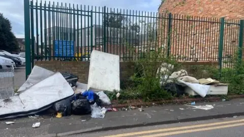 Central Medical Centre Fly-tipped rubbish on a street near a doctors' surgery. The dumped waste includes a white mattress and black rubbish bags.