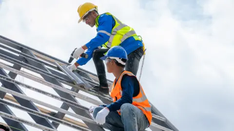 A young roofer pictured alongside a colleague wearing hi-vis jackets