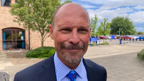 Councillor Adam Kent, wearing a blue suit, and a blue tie.