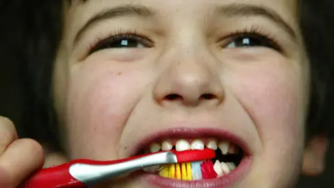 Child brushing teeth with a red toothbrush.