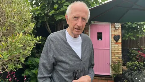 Tony Fisher/BBC Paul Francis standing in his back garden in front of a pink door