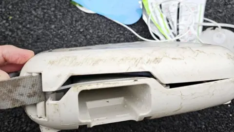 DS43 Community Defibrillators Facebook The side of a defibrillator machine with mud and scratches on it. The top has cables sticking out of it. 