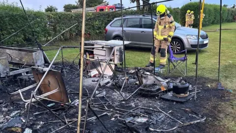 Firefighter standing over a burned tent, which has been destroyed