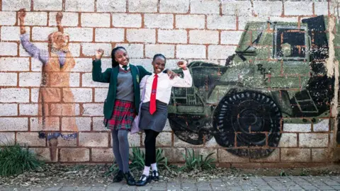 Per-Anders Pettersson/Getty Images Girls pose for pictures at a mural after visiting the Hector Pieterson Museum on June 16, 2024 in Soweto, South Africa. The Soweto Uprising began on June 16, 1976, as a peaceful student protest against the enforcement of Afrikaans in schools. The police and army's response with tear gas and bullets led to violent clashes, resulting in the deaths of 400 to 700 people, many of them children. The event galvanized international opposition to apartheid and is commemorated annually in South Africa as Youth Day.