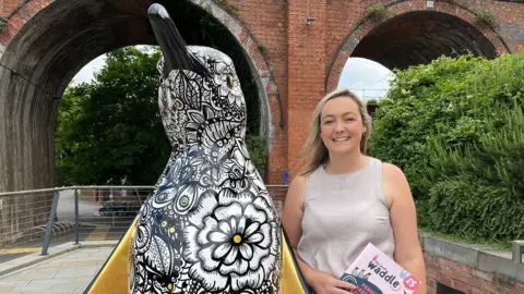 BBC A woman stood next to a penguin sculpture