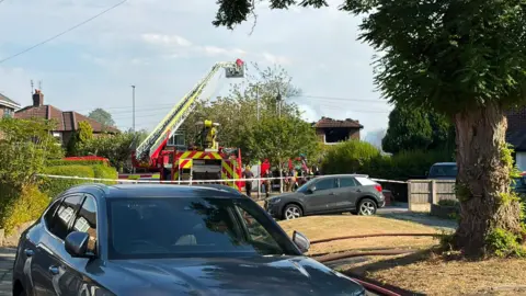 A turntable ladder at the scene of a fire in Northenden. It can be seen extended above a 1930s semi-detached house, the roof of which has collapsed. 