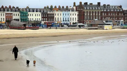 Getty Images Weymouth beach with the promenade in the background. The beach is deserted with the exception of a man and his two dogs