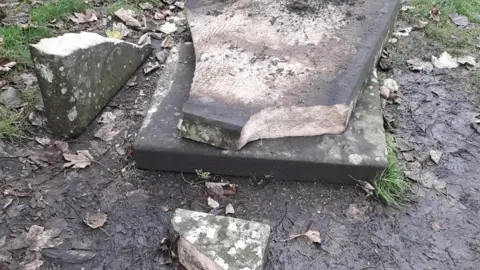 Helen Ball A gravestone on a patch of muddy ground is seen broken into a number of pieces.