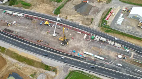 HS2 An aerial view of a construction site with cranes over a dual carriageway.