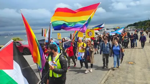 A general view of the Pride march in Brodick with a number of people carrying rainbow flags.