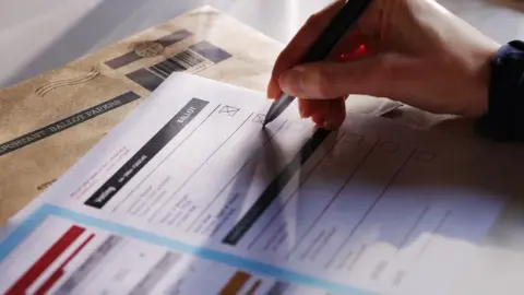 Getty Images A close-up shot of a ballot paper with an unknown person's right hand holding a pen and marking an X on the paper. Only the hand is visible.
