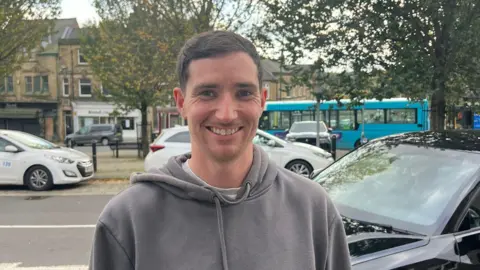 BBC/Georgia Collins Alex Miller, who wears a grey hoodie, seen smiling in the street in Birstall.