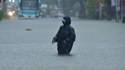Hindustan Times via Getty Images a man who wears a black cloak passes through water in the knee in Mumbai, Maharashtra.