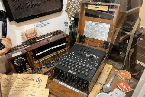 An Engima machine on display in a museum surrounded by other items relating to the German Occupation of Jersey.