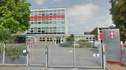 Google A screenshot from Google street view showing a tall while school building behind a closed silver gate.