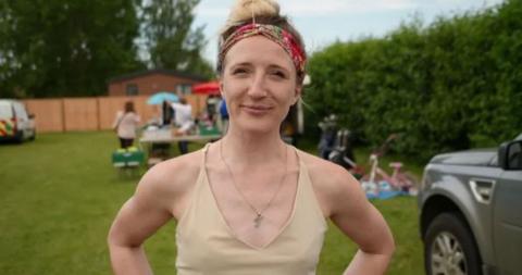 A woman in a cream top and colourful hairband standing outside at a carboot sale