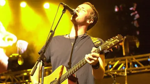 Chris Martin of Coldplay performing on stage with an acoustic guitar in 2000