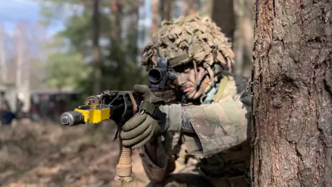 Private Leo Lightbown from South Wigston in full camouflage next to a tree.  