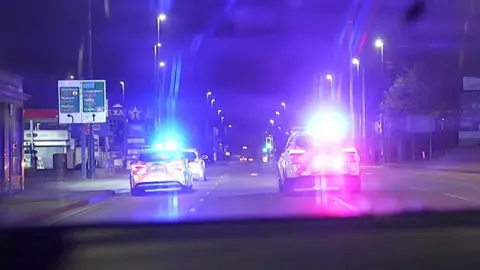 Two police cars with blue lights follow a car that has been racing on a dual carriageway