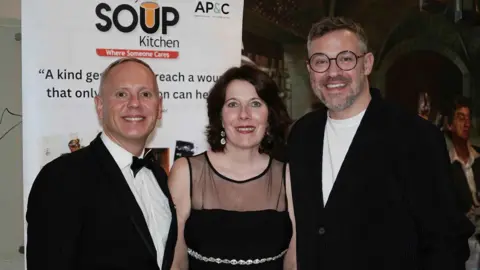 Elizabeth Vickers photogaphy (L-R) Rob Rinder smiling at the camera is wearing a black dress suit and bow tie, Newbury Soup Kitchen chief executive Meryl Praill is smiling at the camera wearing a black evening dress and Will Young is smiling and wearing a white t-shirt and black cardigan.