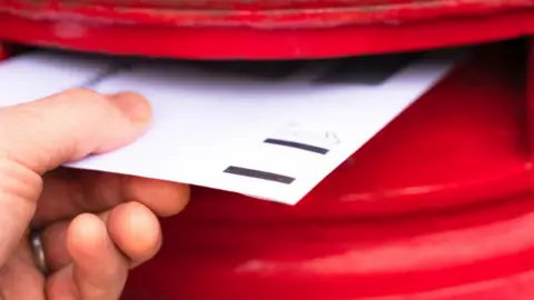 A white letter is put into a red letterbox in a close-up image.