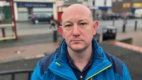 A man in a bright blue jacket stands in Featherstone
