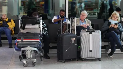 People sit inside an airport with their luggage.