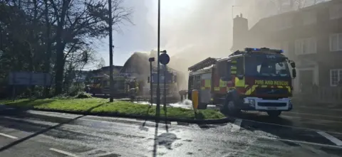 HIWFRS Fire engines on a road with a building behind them covered in thick smoke.