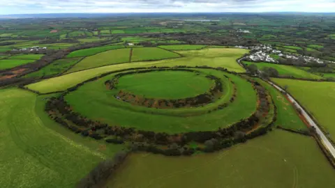 A drone shot of the circular fort. It is grassy and surrounded by numerous fields.