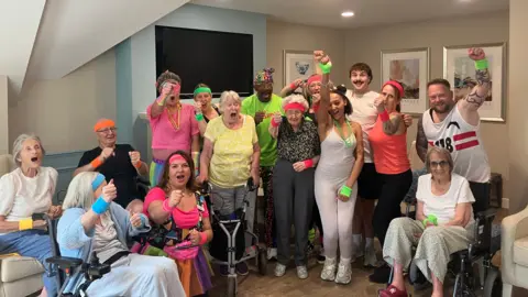 Care home residents and staff at Lindley Park pose for a photo with Mr Motivator while wearing bright-coloured head and wrist bands.