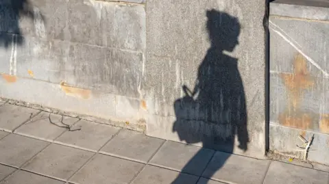 Getty Images Shadow of a child on the concrete as they walk down the street, looks like they are wearing a rucksack and are on their own