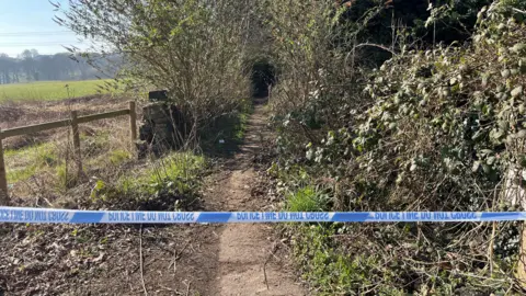 BBC/Adam Laver Police tape in front of entrance to wooded area