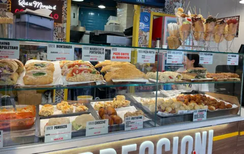 Food stall in Napoli with shelves stocked with sandwiches, pasta, bread, and fried foods