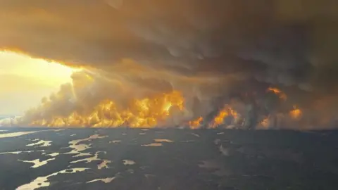 A handout photo made available by the government of Manitoba shows a large wildfire near Flin Flon, Manitoba, Canada. It shows woods and flames with large plumes of smoke filling the sky 