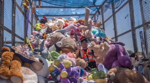 Brenton Geach /  Getty Images A man arranges a huge mass of plush toys on the back of a lorry.